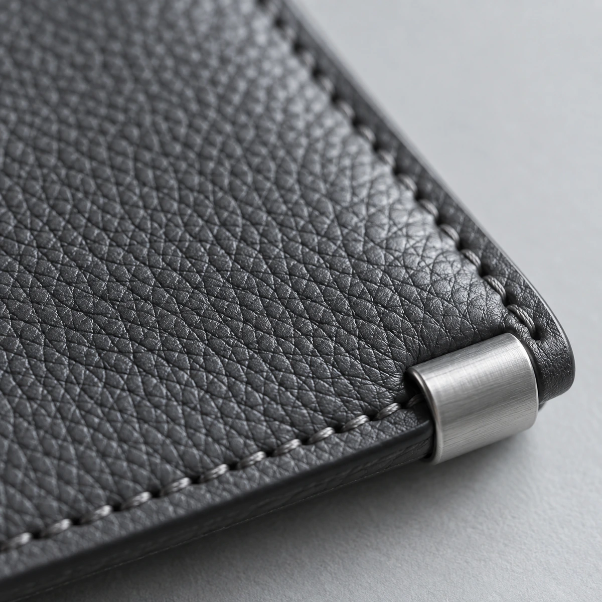 Close-up of graphite leather grain, edge stitching and a brushed-metal fitting.